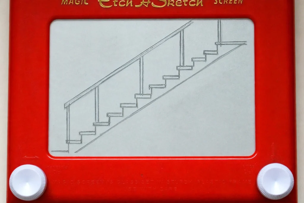 Close-up of the two white knobs and the grey screen of a red Etch A Sketch with a staircase drawing