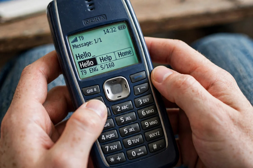 Hands typing a text message using T9 predictive text on an old Nokia keypad